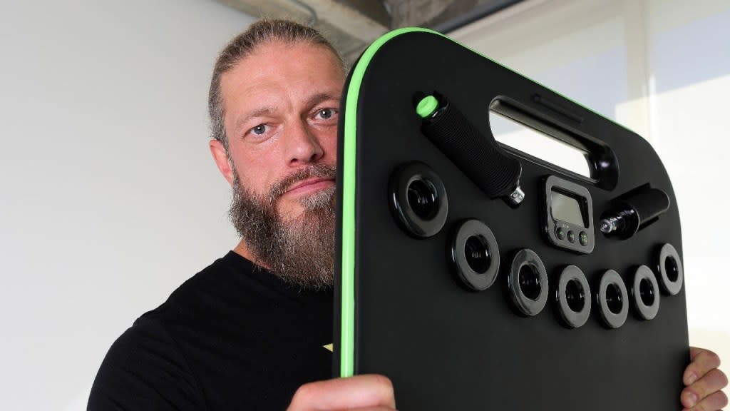Man holding a black fitness device with handles and a display screen.