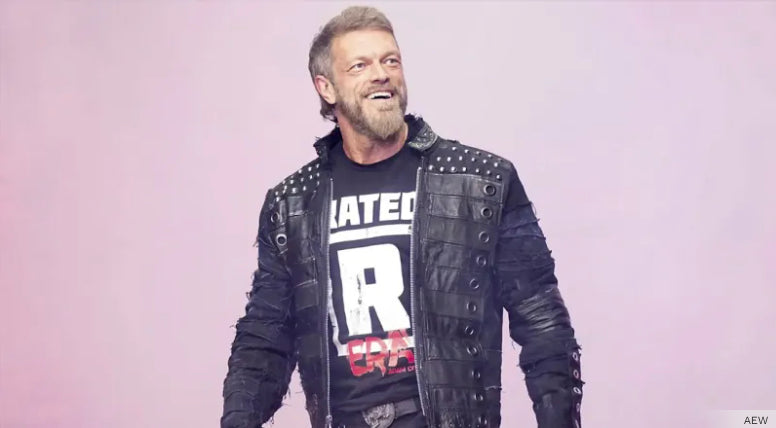Man in a studded jacket and graphic t-shirt, smiling against a light background.